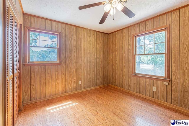 spare room with crown molding, ceiling fan, wooden walls, light hardwood / wood-style floors, and a textured ceiling