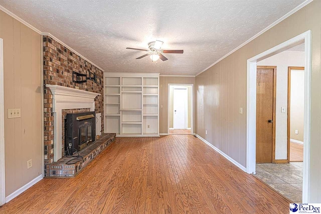 unfurnished living room with a fireplace, wood-type flooring, ceiling fan, crown molding, and a textured ceiling