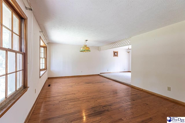 empty room featuring a chandelier, hardwood / wood-style floors, and a textured ceiling