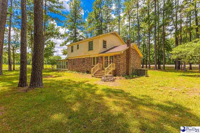 rear view of house featuring a yard, a sunroom, and central air condition unit