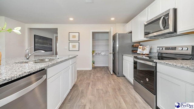 kitchen with white cabinets, light stone countertops, light wood-style floors, appliances with stainless steel finishes, and a sink