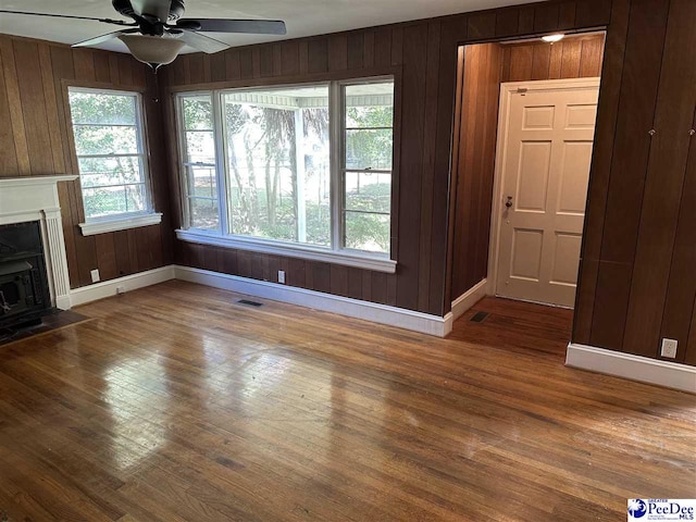 unfurnished living room featuring ceiling fan, hardwood / wood-style floors, and wooden walls