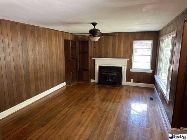 unfurnished living room with dark hardwood / wood-style floors, ceiling fan, and wood walls