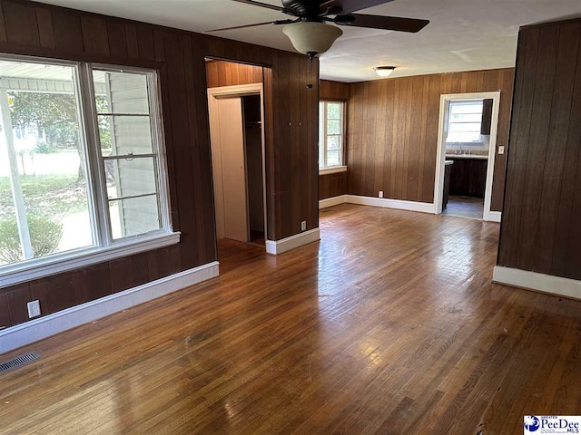 unfurnished room with dark wood-type flooring, ceiling fan, and wooden walls