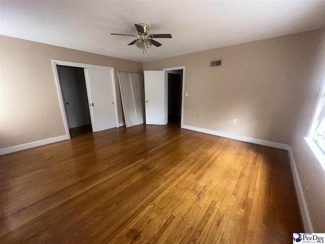 unfurnished bedroom featuring multiple closets, hardwood / wood-style flooring, and ceiling fan