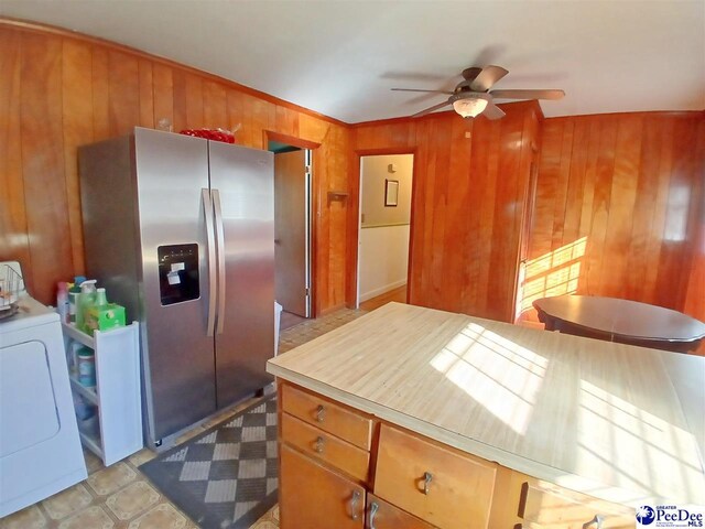 kitchen featuring ceiling fan, wooden walls, washer / dryer, and stainless steel fridge with ice dispenser