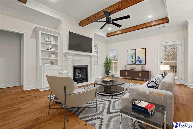 living room with built in features, ornamental molding, ceiling fan, light hardwood / wood-style floors, and beam ceiling