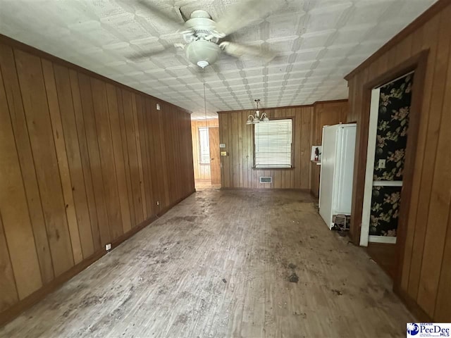 unfurnished living room featuring wooden walls, an ornate ceiling, a ceiling fan, baseboards, and light wood-type flooring
