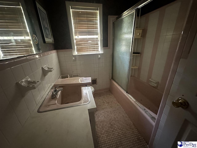 full bath with tile walls, wainscoting, bath / shower combo with glass door, vanity, and toilet