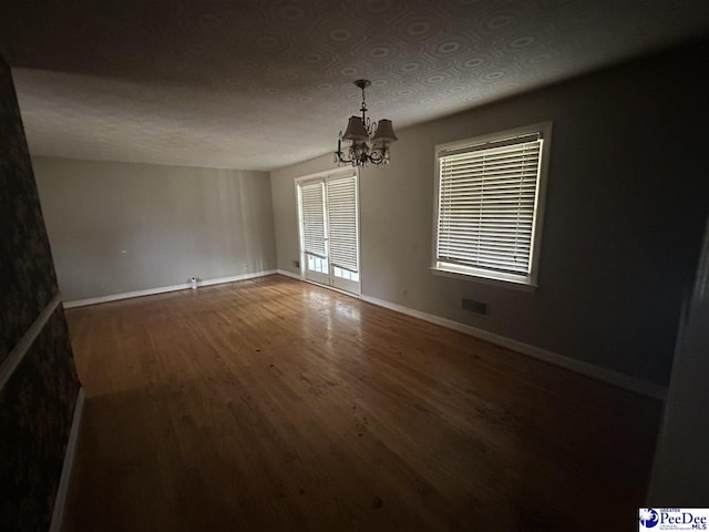 unfurnished dining area with baseboards, visible vents, wood finished floors, and a chandelier