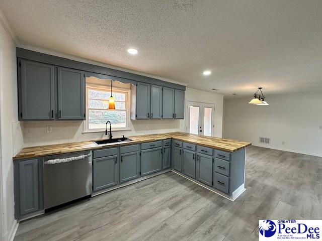 kitchen featuring light wood-type flooring, decorative light fixtures, sink, dishwasher, and wood counters