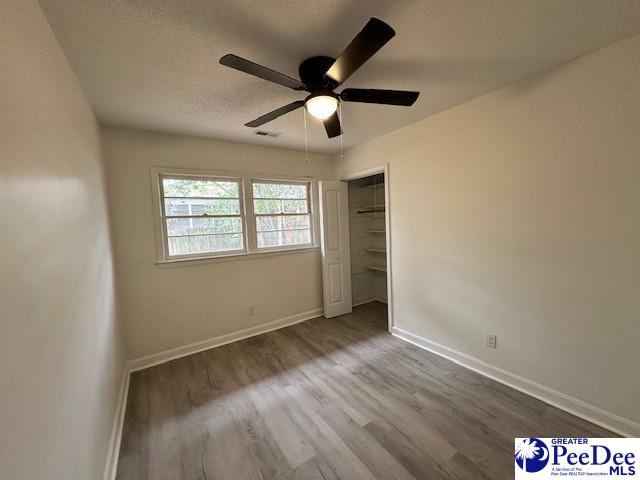 unfurnished bedroom with ceiling fan, a closet, wood-type flooring, and a textured ceiling