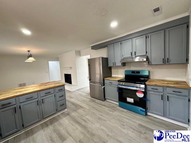 kitchen with light wood-type flooring, appliances with stainless steel finishes, butcher block countertops, and pendant lighting