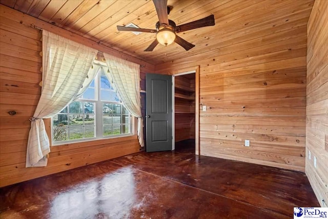 interior space featuring concrete flooring, a ceiling fan, wood ceiling, and wooden walls