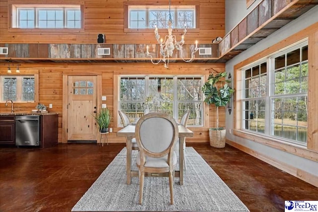 unfurnished dining area featuring wood walls, visible vents, a high ceiling, and a chandelier