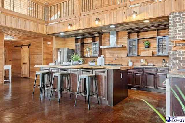 kitchen with wooden walls, appliances with stainless steel finishes, light countertops, wall chimney range hood, and a kitchen bar