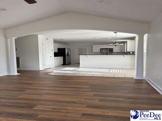 unfurnished living room featuring dark hardwood / wood-style flooring, vaulted ceiling, ceiling fan, and ornate columns