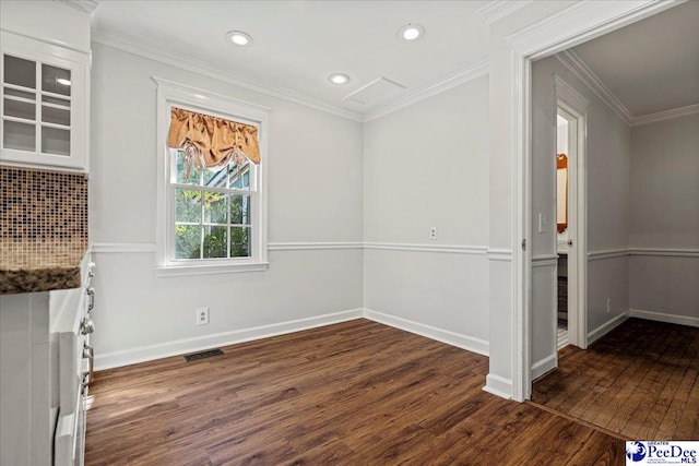 unfurnished dining area with dark wood-type flooring, visible vents, crown molding, and baseboards