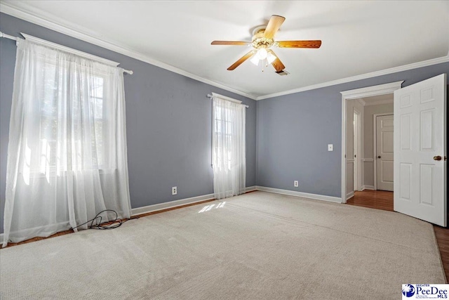 empty room with a ceiling fan, carpet, crown molding, and baseboards