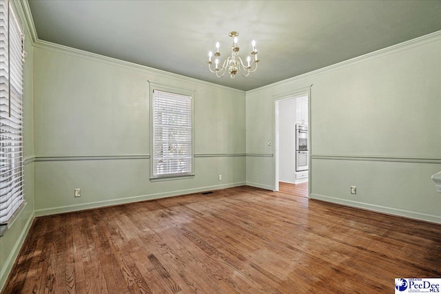 spare room featuring an inviting chandelier, crown molding, baseboards, and wood finished floors