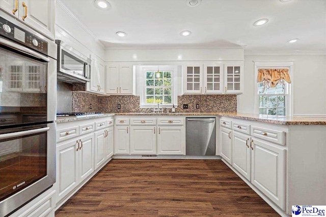 kitchen with white cabinets, dark wood finished floors, glass insert cabinets, appliances with stainless steel finishes, and crown molding