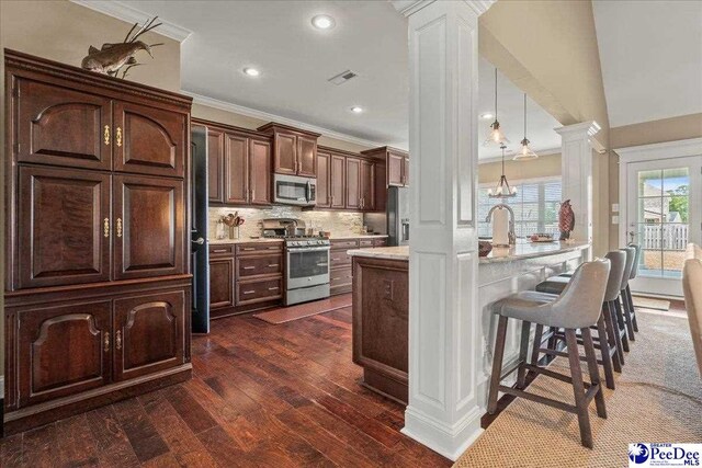 3111 Cheshire Ln, Florence, SC 29501 - kitchen with appliances with stainless steel finishes, ornate columns, ornamental molding, a breakfast bar area, and light countertops