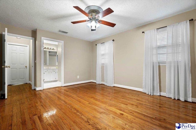 unfurnished bedroom featuring connected bathroom, wood-type flooring, a textured ceiling, and ceiling fan