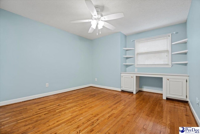 unfurnished bedroom with ceiling fan, built in desk, a textured ceiling, and light wood-type flooring