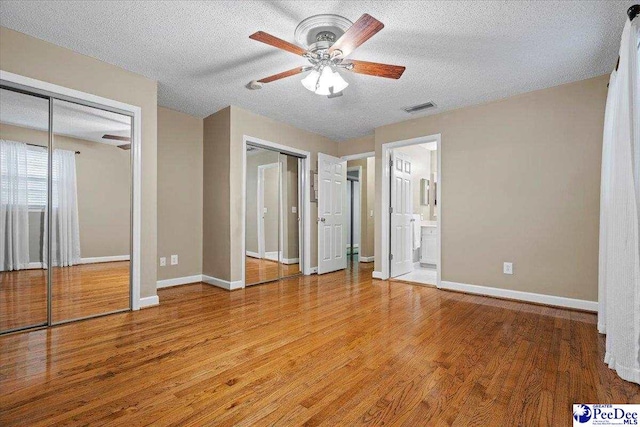 unfurnished bedroom with ensuite bathroom, hardwood / wood-style flooring, ceiling fan, multiple closets, and a textured ceiling