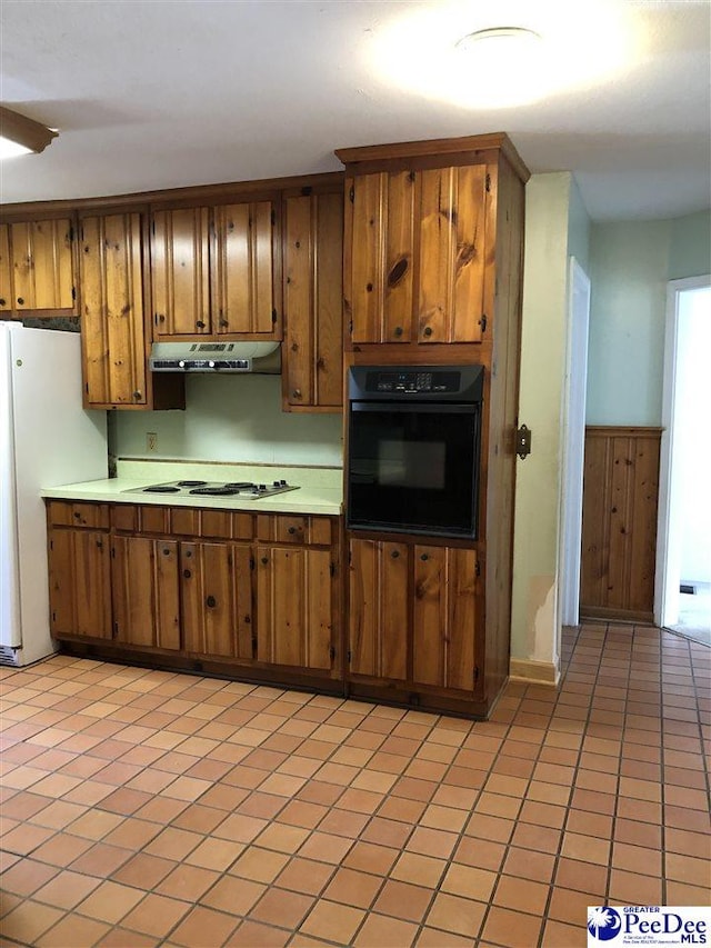 kitchen featuring electric cooktop, brown cabinets, freestanding refrigerator, under cabinet range hood, and black oven