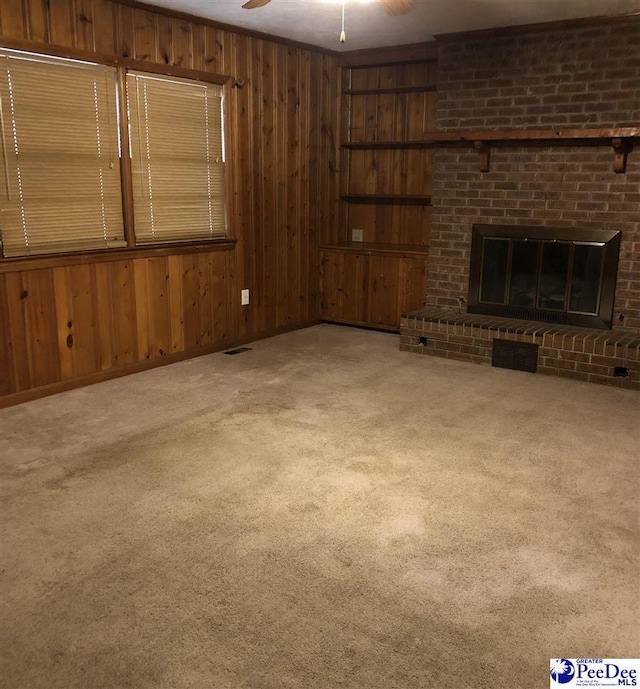 unfurnished living room with carpet floors, a brick fireplace, wooden walls, and a ceiling fan