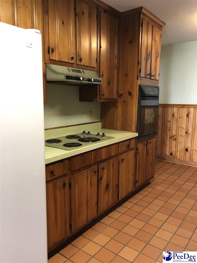 kitchen featuring wainscoting, electric stovetop, oven, freestanding refrigerator, and under cabinet range hood