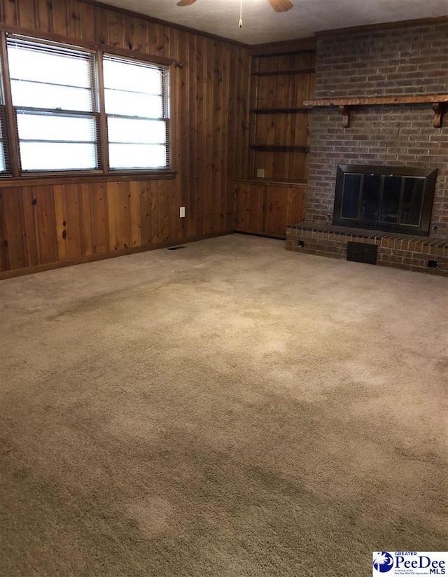 unfurnished living room featuring built in shelves, carpet, a fireplace, a ceiling fan, and wooden walls