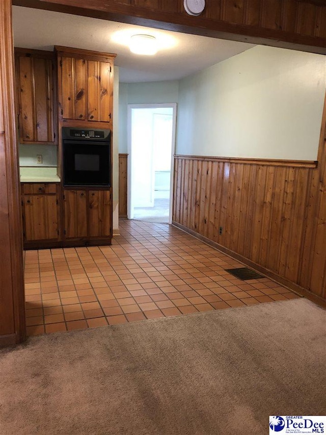 kitchen featuring brown cabinets, wainscoting, light colored carpet, and black oven