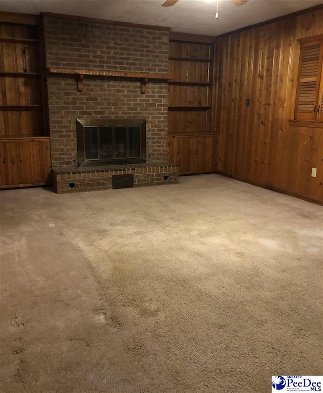 unfurnished living room with a brick fireplace, wooden walls, a ceiling fan, and carpet flooring