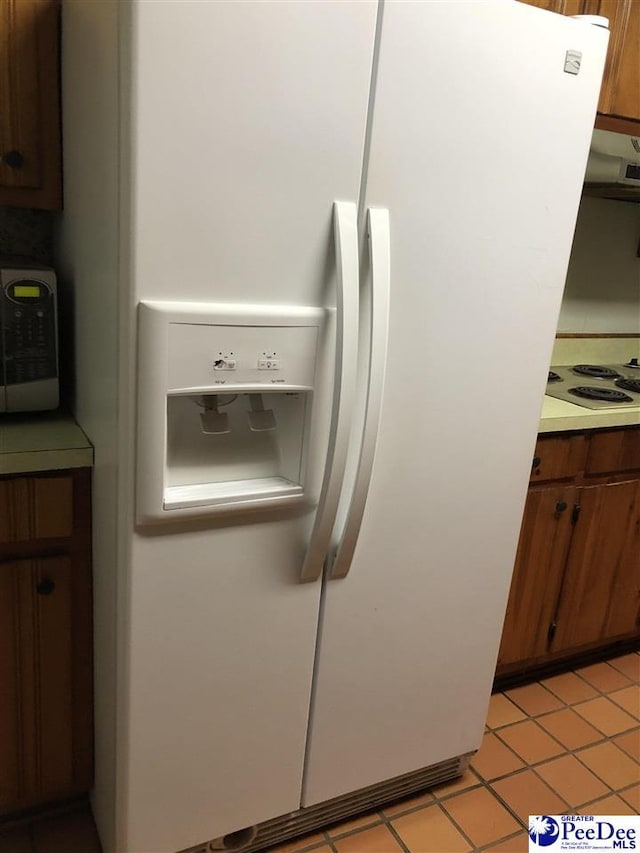 interior details with white refrigerator with ice dispenser, brown cabinets, light countertops, electric stovetop, and exhaust hood