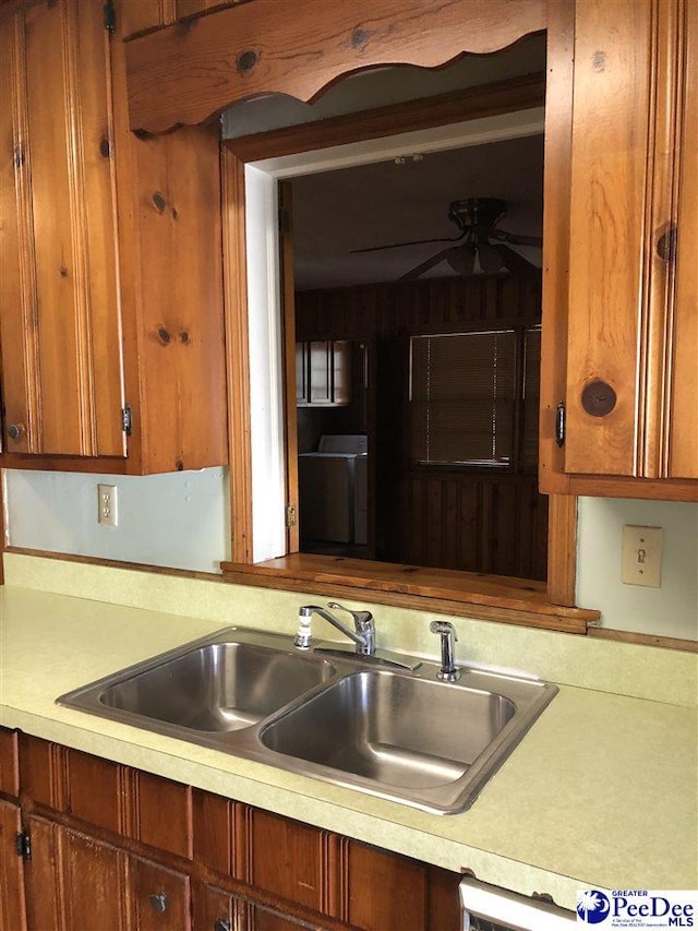 kitchen with brown cabinets, light countertops, a ceiling fan, a sink, and washer / dryer