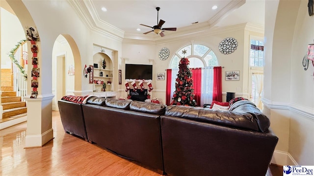 living room with crown molding, ceiling fan, built in shelves, light wood-type flooring, and ornate columns