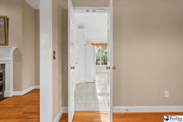 hall featuring baseboards, light wood-style floors, and crown molding
