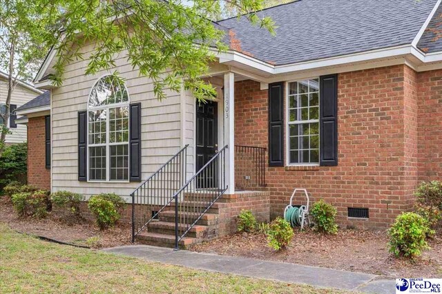 doorway to property featuring brick siding, crawl space, and roof with shingles