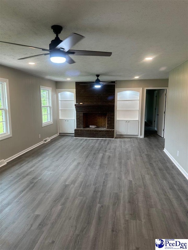 unfurnished living room featuring a fireplace, dark wood-type flooring, built in features, and a textured ceiling