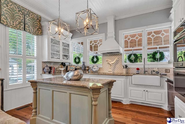 kitchen with premium range hood, light stone countertops, a center island, and hanging light fixtures