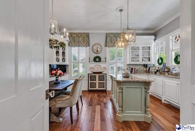 kitchen with dark wood-type flooring, white cabinetry, hanging light fixtures, a kitchen island, and light stone countertops