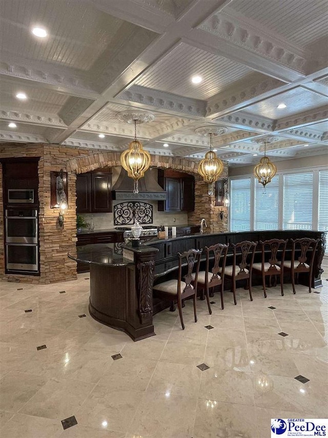 bar with stainless steel double oven, coffered ceiling, hanging light fixtures, and custom range hood