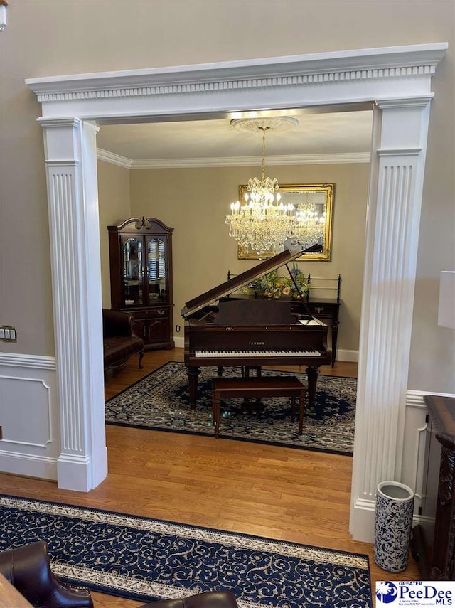 misc room with a notable chandelier, hardwood / wood-style flooring, ornamental molding, and decorative columns