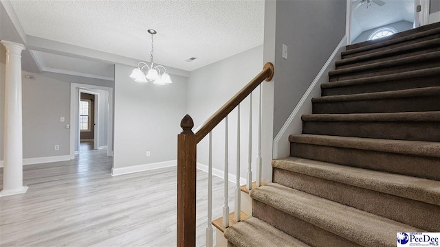 stairway featuring decorative columns, wood-type flooring, a chandelier, and a textured ceiling