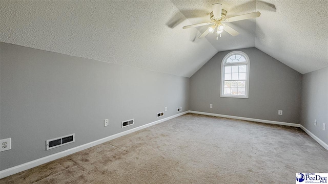 additional living space with ceiling fan, lofted ceiling, light colored carpet, and a textured ceiling