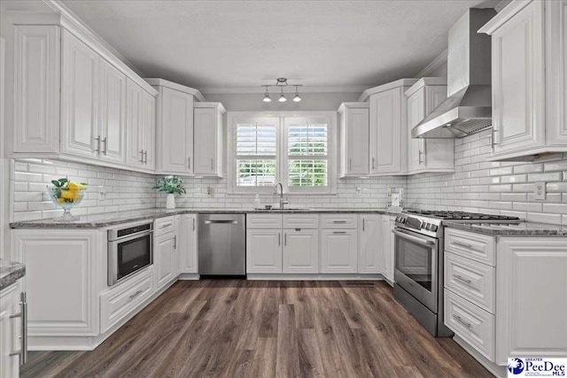 100 Mckellar St, Bennettsville, SC 29512 - kitchen with appliances with stainless steel finishes, wall chimney exhaust hood, a sink, white cabinets, and dark wood-style flooring