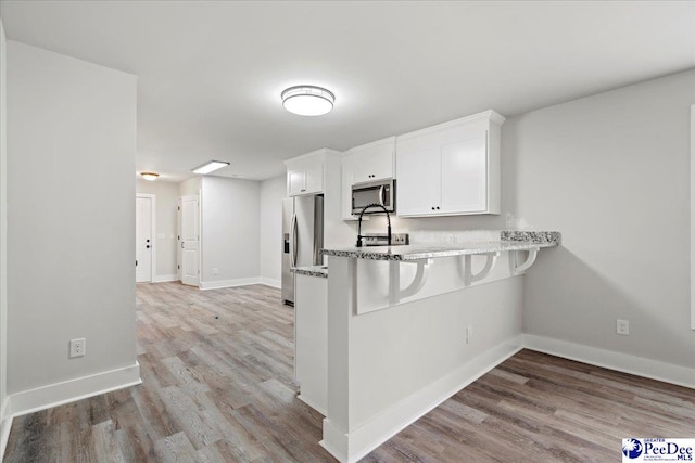 kitchen with white cabinetry, kitchen peninsula, stainless steel appliances, light stone countertops, and light wood-type flooring