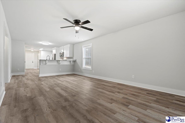 unfurnished living room with hardwood / wood-style flooring, sink, and ceiling fan